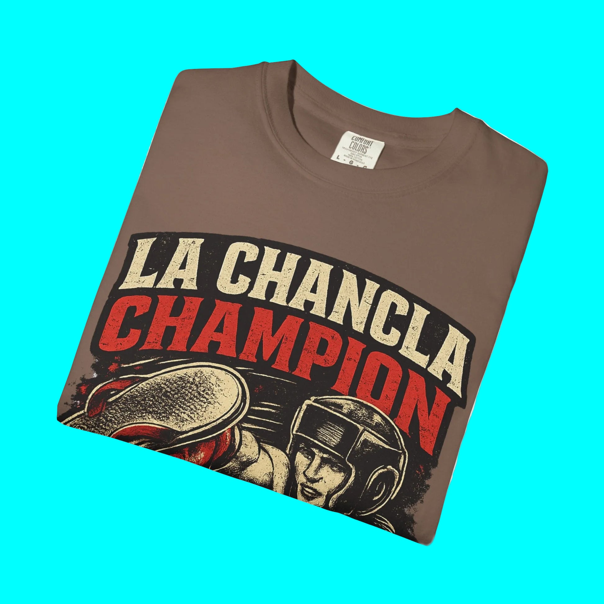 Folded brown t-shirt with 'La Chancla Champion' graphic design on a white background