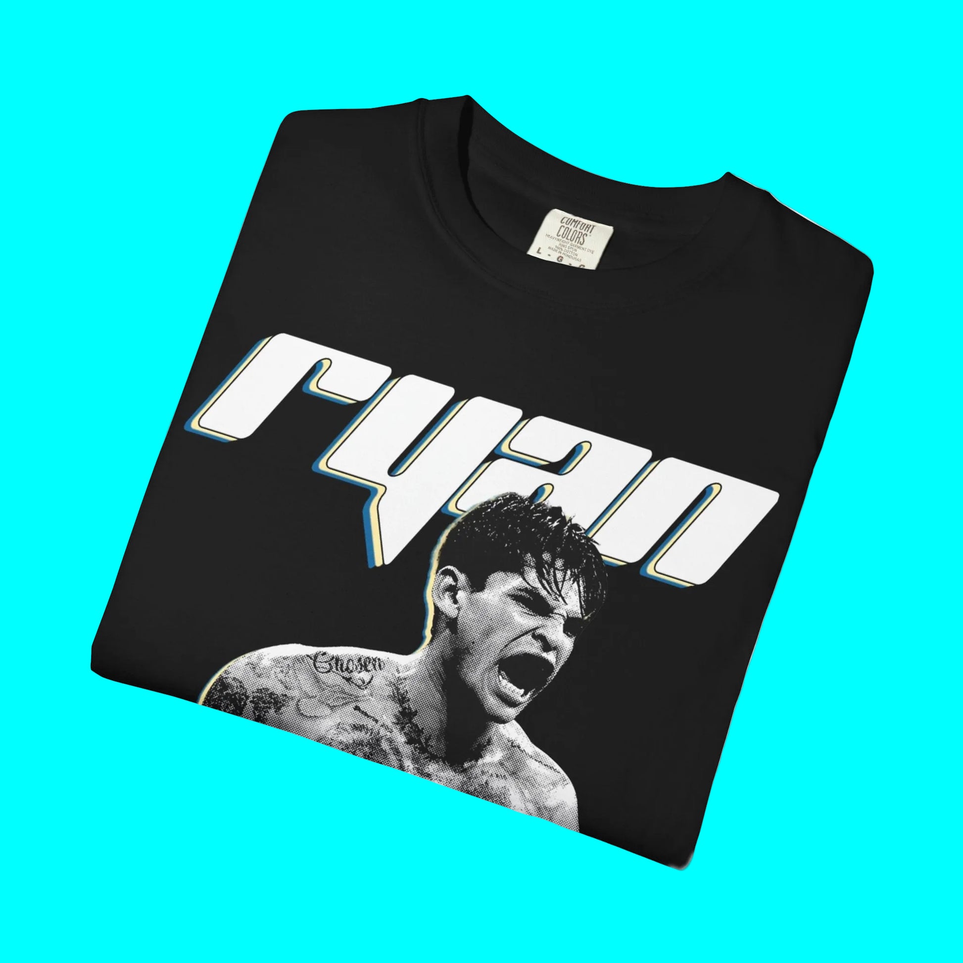 A folded black t-shirt featuring a large white 'ryan' graphic with a blue and yellow outline, and a black-and-white photo of a screaming tattooed man below it, shown on a plain white background.