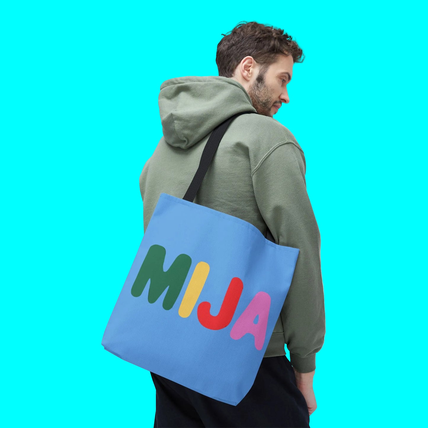 Person wearing a green hoodie with a blue tote bag featuring colorful letters 'MIJA' on a white background