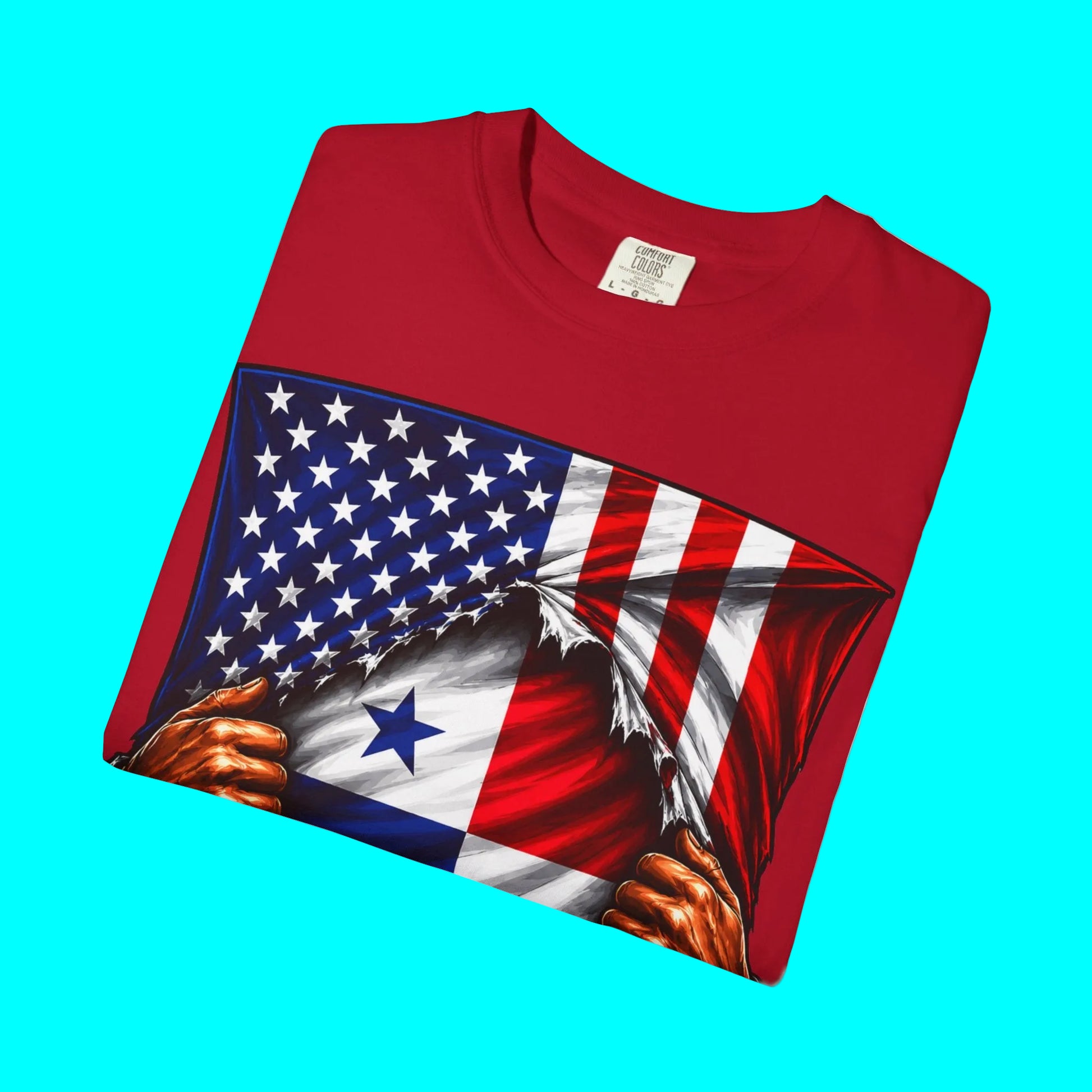 A folded red crewneck t-shirt featuring a graphic print of a patriotic American flag with a torn effect revealing the flag of Panama underneath, including two hands tearing the fabric.