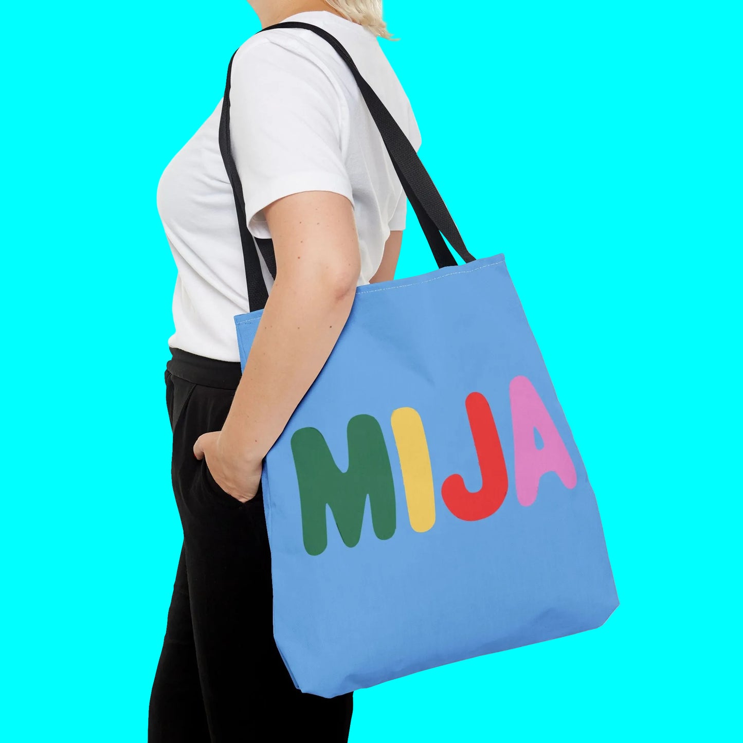 Person holding a blue tote bag with colorful letters spelling 'MIJA' on a white background