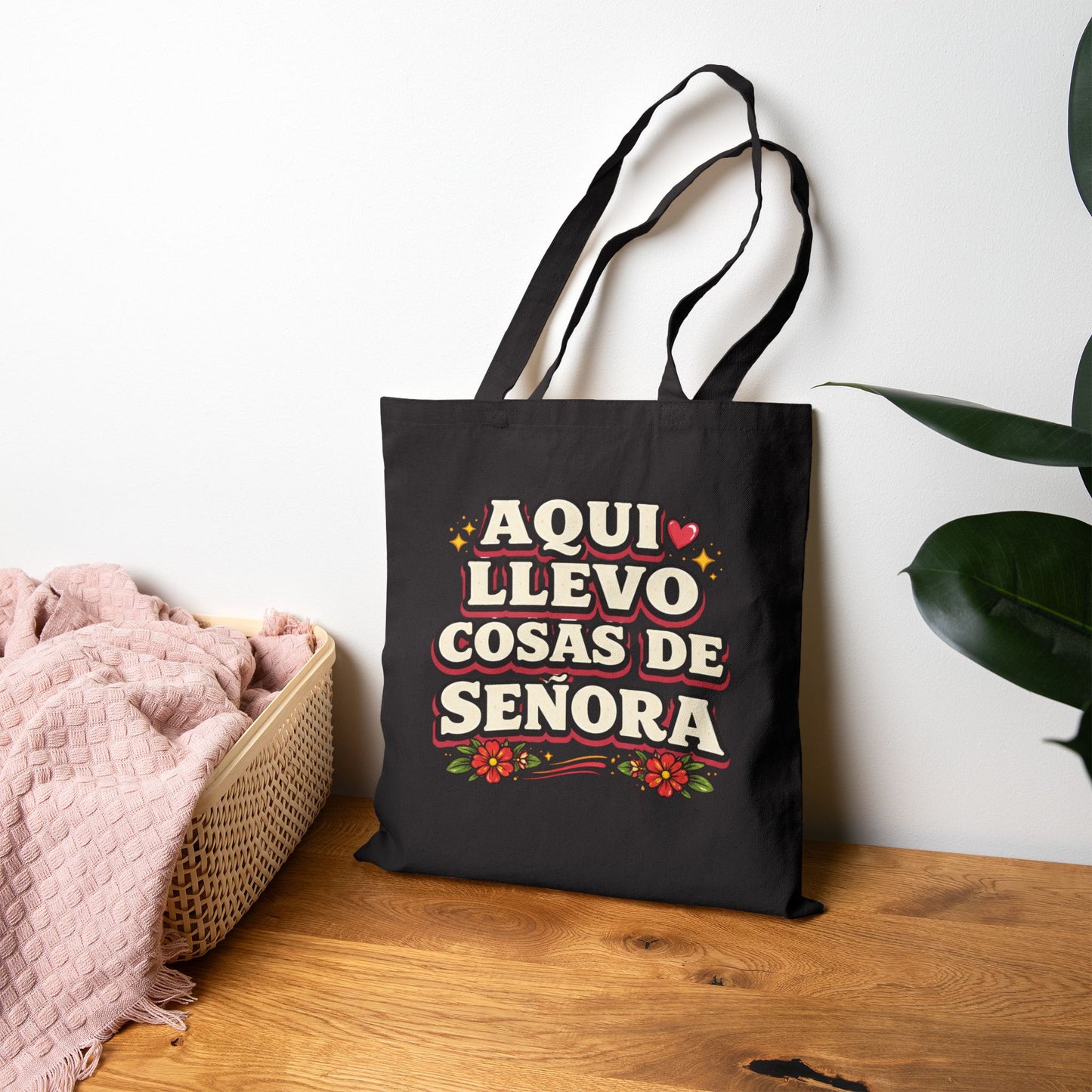 Black tote bag with colorful text and graphics on a wooden surface with a white wall background.