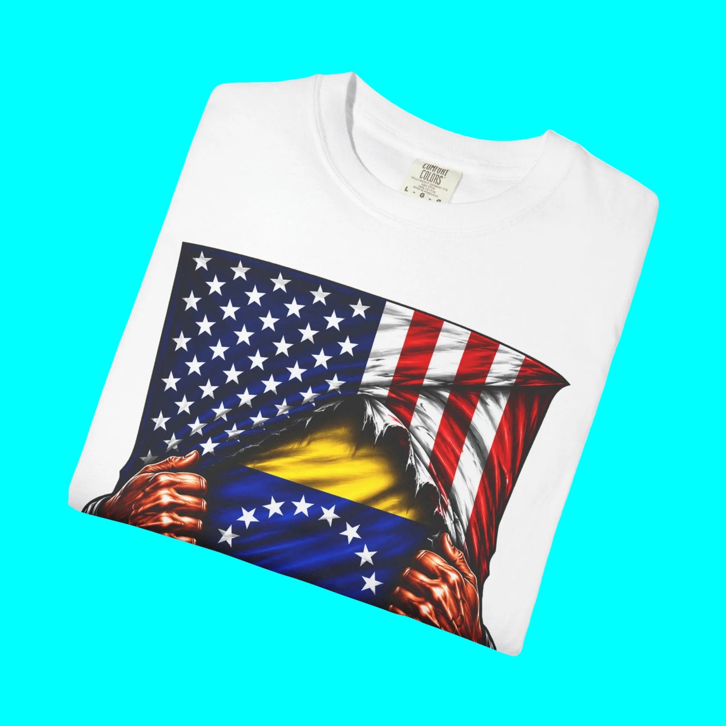 A folded white crewneck t-shirt featuring a graphic print of a patriotic American flag with a blue section showing the yellow and red stripes of the Venezuelan flag, with red hands tearing the fabric.