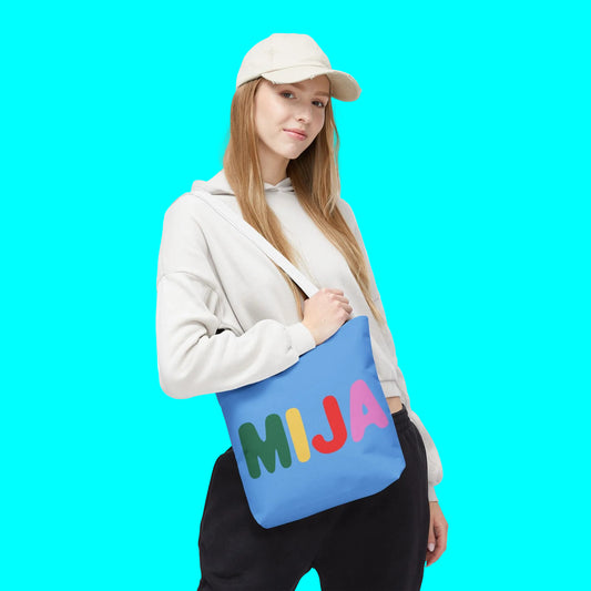Person holding a blue tote bag with colorful 'MIJA' letters on a white background