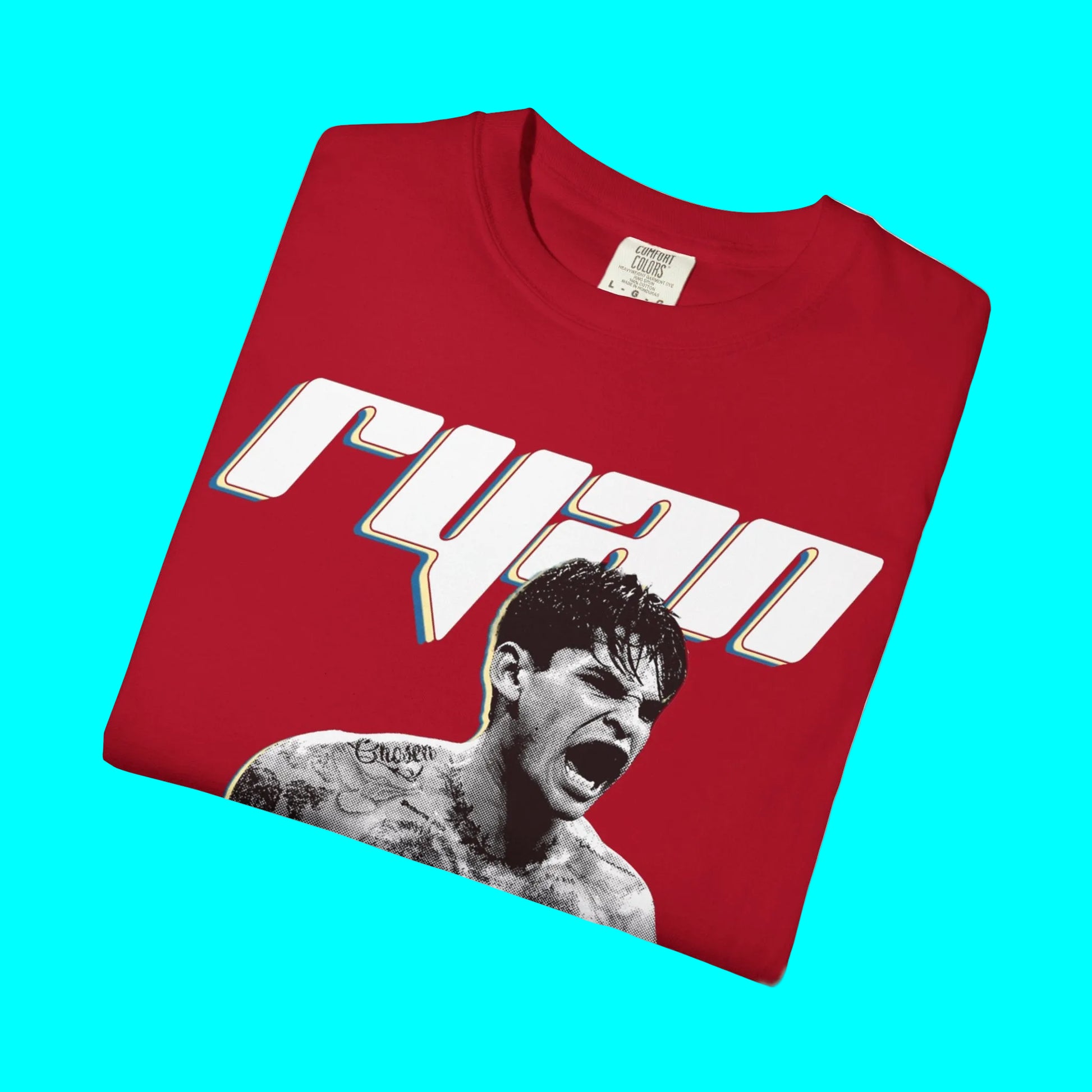A folded red t-shirt with a graphic print featuring the name 'ryan' in stylized white letters with a thin blue and yellow outline, and a black-and-white portrait of a screaming man below it, shown on a plain white background.