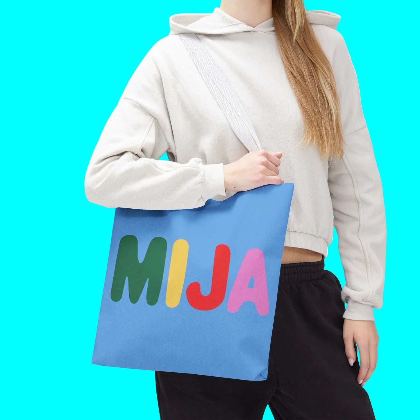 Person holding a blue tote bag with colorful letters 'MIJA' on a white background