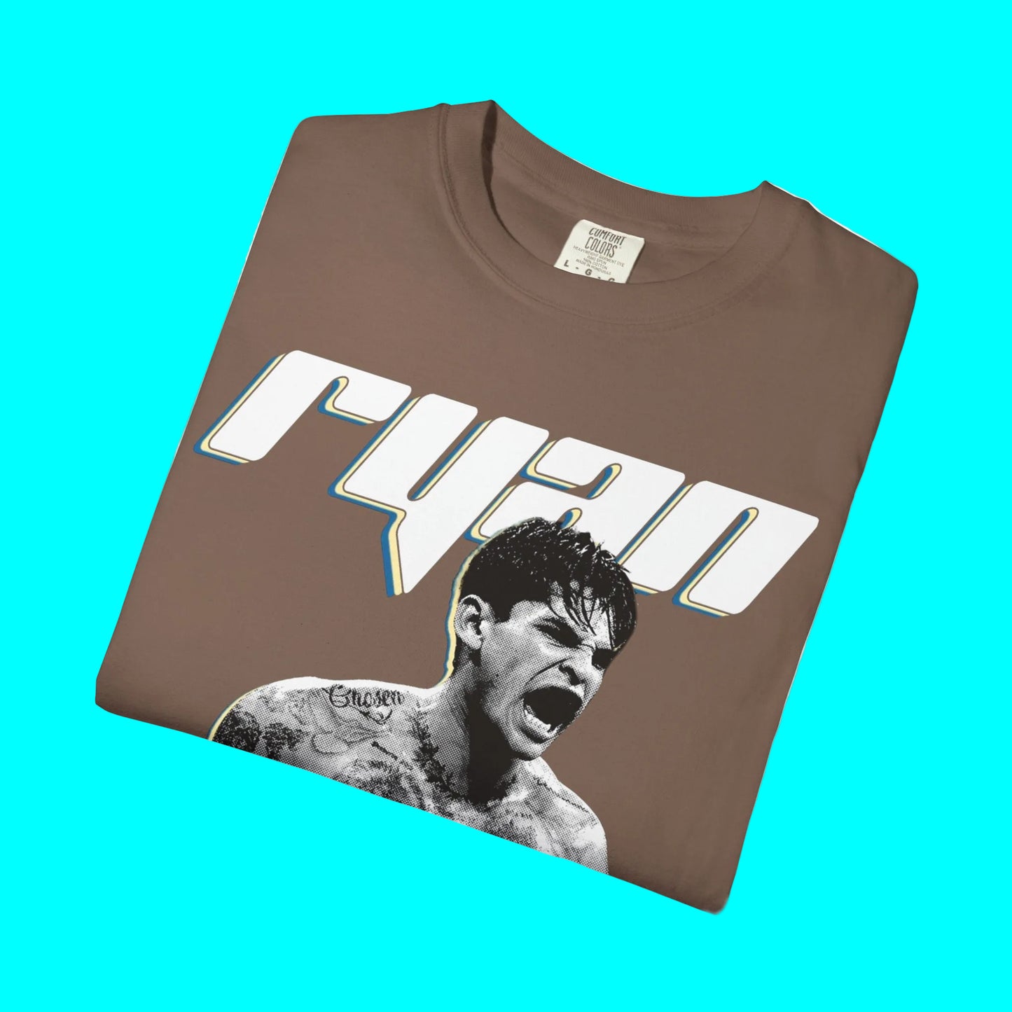 A brown folded t-shirt featuring a graphic print of the name 'ryan' in a stylized white font with a blue and yellow outline, and a black-and-white photo of a screaming man with tattoos below it.