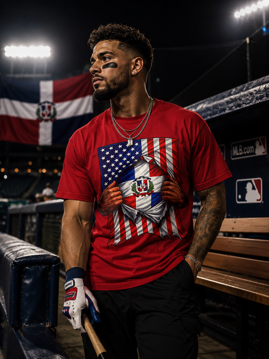 Person wearing a red t-shirt with an American and Dominican flag design, holding a baseball bat in a stadium setting.