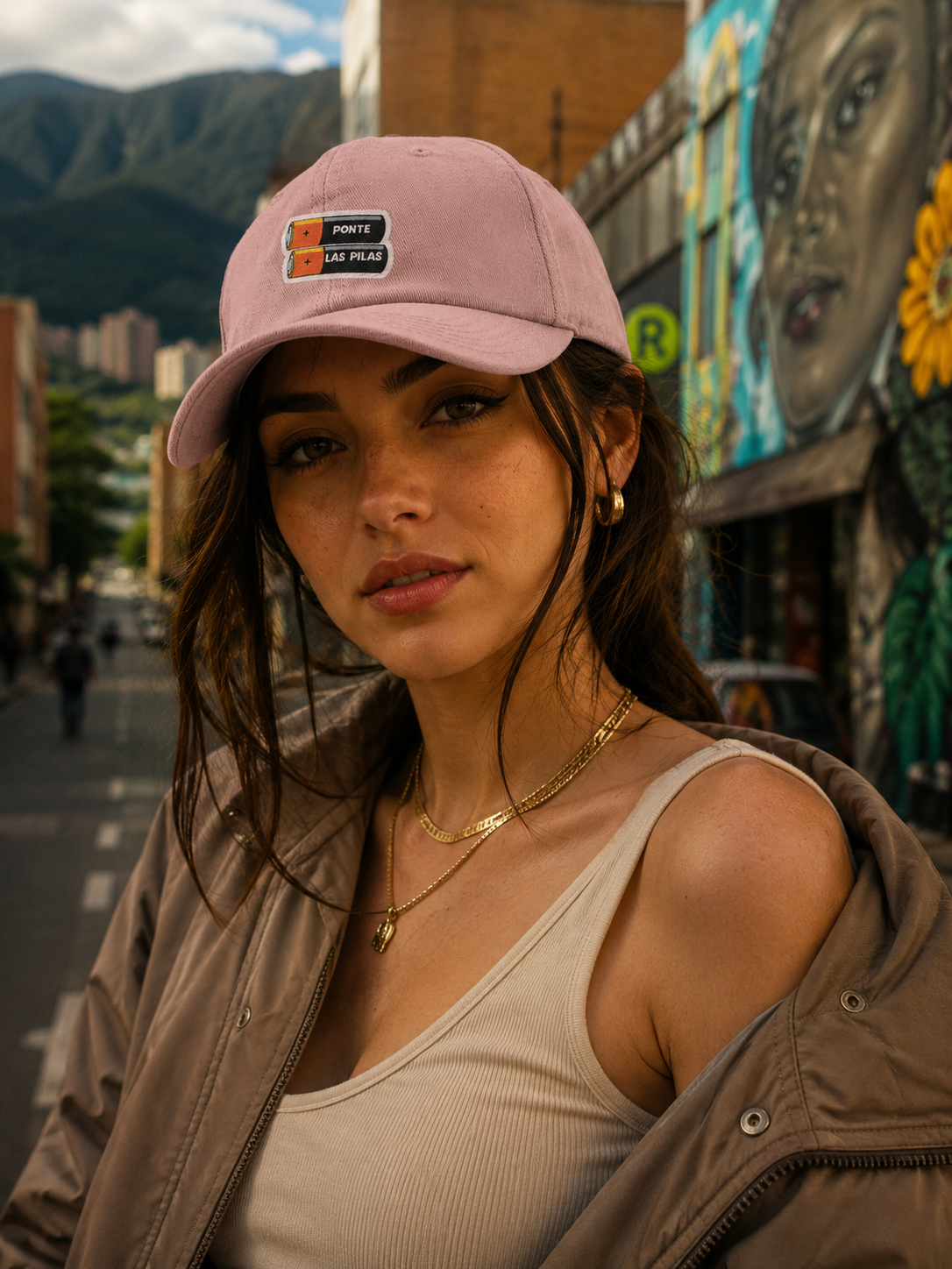 Woman wearing a pink cap with patches in an urban setting with mountains in the background.