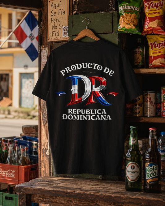 A black t-shirt hanging on a wooden hanger in a rustic shop setting, featuring a large graphic on the back with the text 'PRODUCTO DE REPUBLICA DOMINICANA' and a stylized 'DR' in the colors of the Dominican flag.