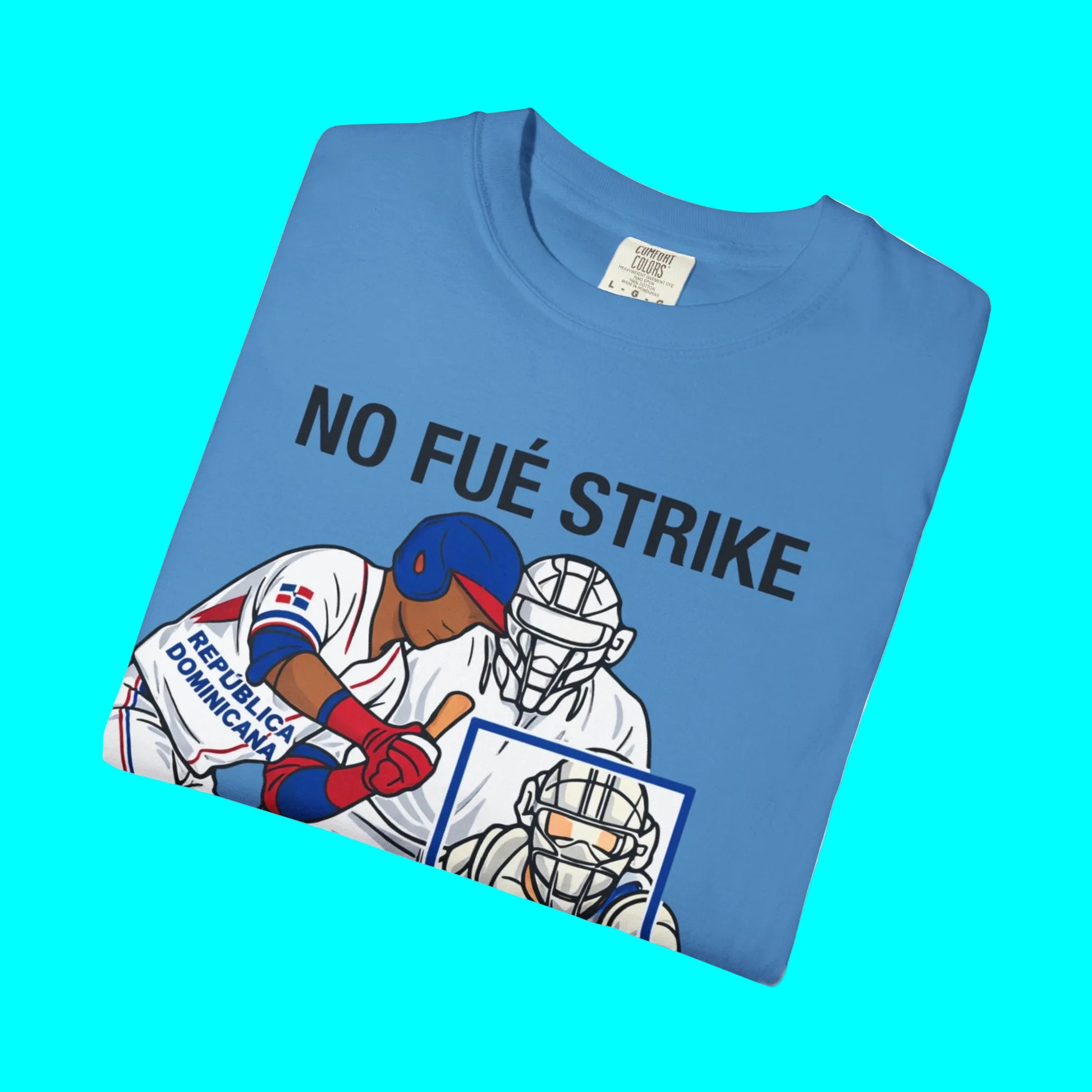 Folded blue t-shirt with graphic of baseball players and 'NO FUÉ STRIKE' text on a white background