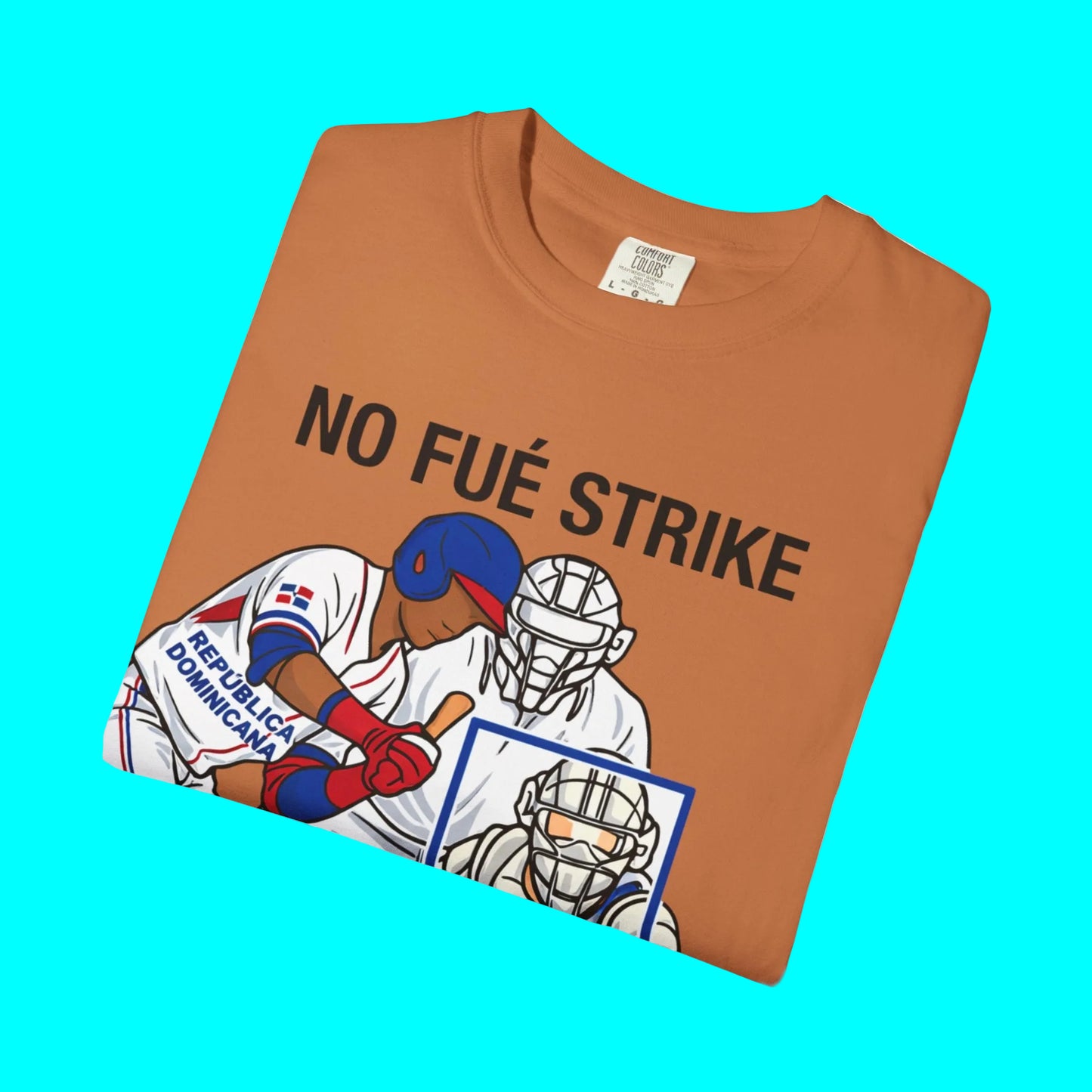Folded brown t-shirt with graphic of baseball players and 'NO FUÉ STRIKE' text on a white background