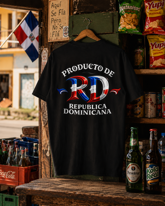 A black short-sleeve t-shirt hanging on a wooden hanger in a rustic shop setting, featuring a large graphic on the back with the text 'PRODUCTO DE REPUBLICA DOMINICANA' and a stylized 'RD' in the colors of the Dominican flag.